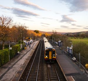 A train travelling through the Hope Valley railway line, with the sun shining down upon it.