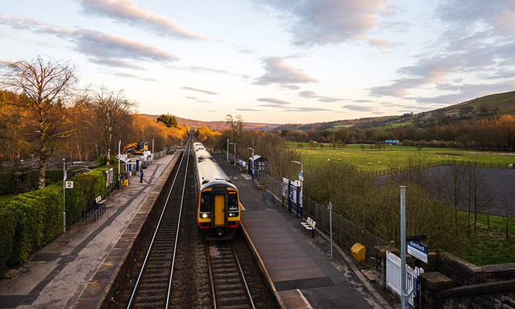 A train travelling through the Hope Valley railway line, with the sun shining down upon it.