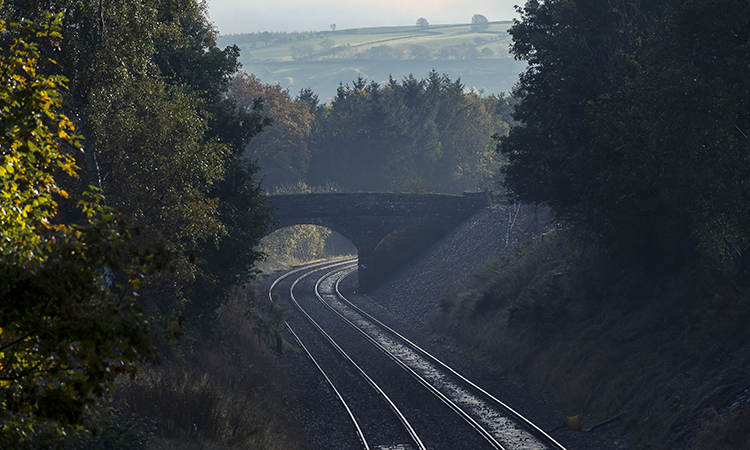 Empty rail track passing beneath a bridge in the English countryside.