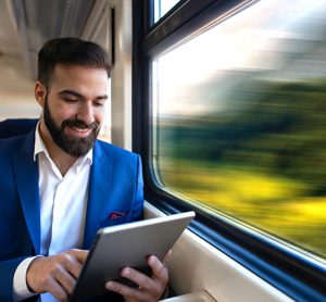 Businessman sitting next to window reading news and surfing internet on his tablet while traveling in comfortable high speed train.