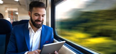 Businessman sitting next to window reading news and surfing internet on his tablet while traveling in comfortable high speed train.
