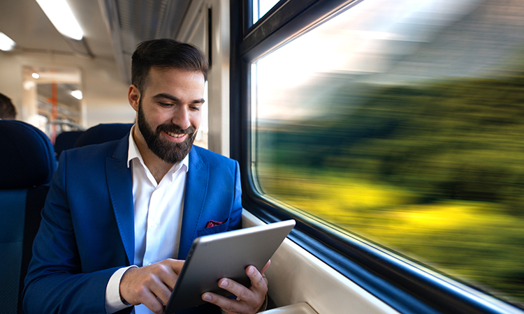 Businessman sitting next to window reading news and surfing internet on his tablet while traveling in comfortable high speed train.