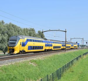 Typical Dutch yellow-blue InterCity VIRM EMU train in green natural environment in sunny weather under blue sky