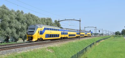 Typical Dutch yellow-blue InterCity VIRM EMU train in green natural environment in sunny weather under blue sky