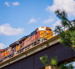 A low angle view of two BNSF locomotives pulling cars over an extremely high viaduct as seen from below.
