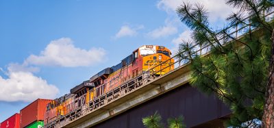 A low angle view of two BNSF locomotives pulling cars over an extremely high viaduct as seen from below.