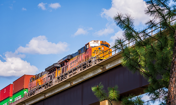 A low angle view of two BNSF locomotives pulling cars over an extremely high viaduct as seen from below.