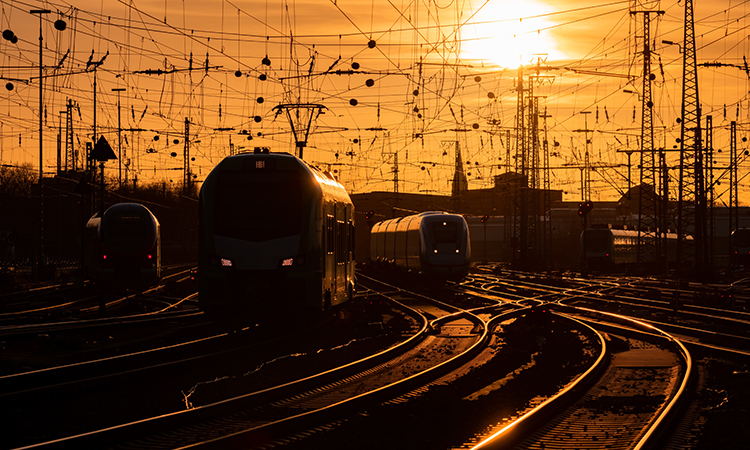 Trains arriving at Dortmund station in warm evening light, with the curved main line railway tracks glistening in the sun.