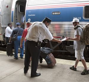 Railroad conductor and station staff assist passengers to board an Amtrak train.