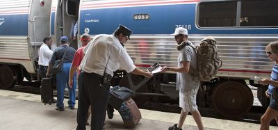 Railroad conductor and station staff assist passengers to board an Amtrak train.