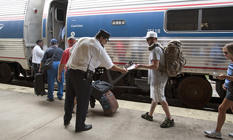 Railroad conductor and station staff assist passengers to board an Amtrak train.