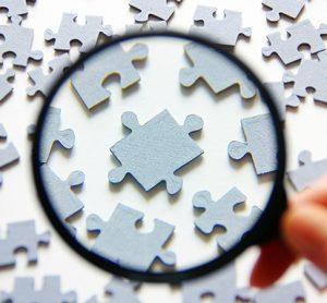 Hand with magnifying glass and puzzle isolated on white background