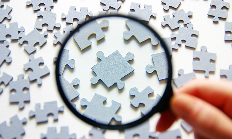 Hand with magnifying glass and puzzle isolated on white background