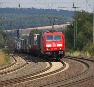 DB (Deutsche Bahn) Modern Locomotive with container wagons drives on tracks.