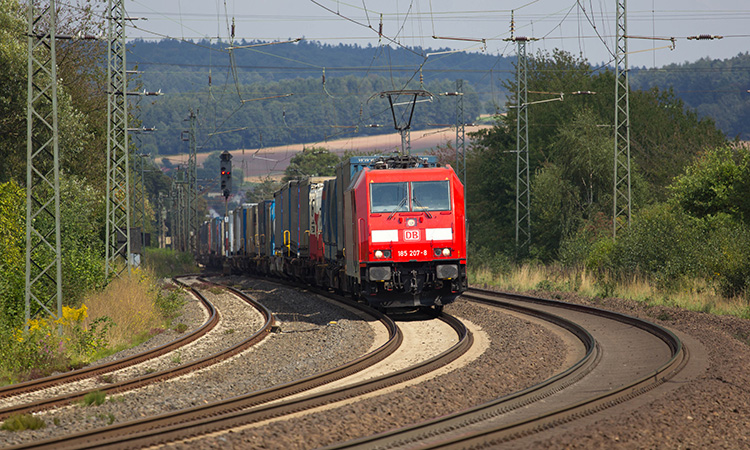 DB (Deutsche Bahn) Modern Locomotive with container wagons drives on tracks.